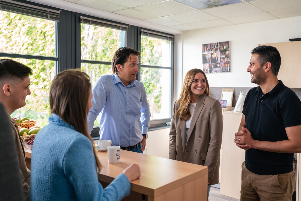 Fünf Personen unterhalten sich stehend in einer modernen Büroküche mit Obstschale.